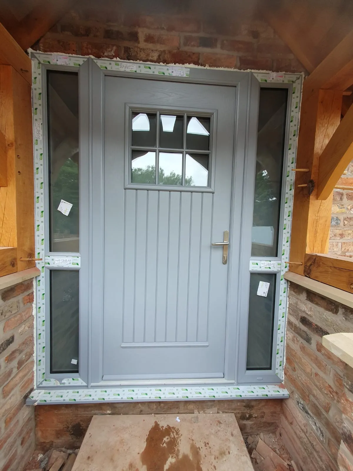 Grey composite cottage-style front door with sidelights inside a stone porch