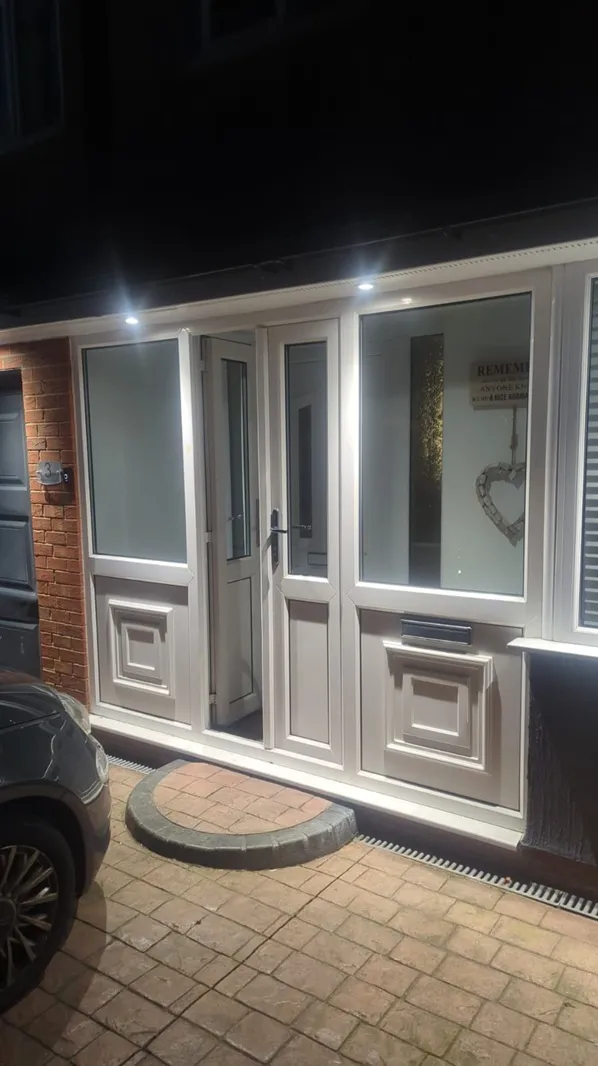 White PVC front porch with panelled door and large glazed side screens at night