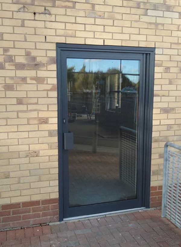 Anthracite grey aluminium single commercial door on a buff brick unit