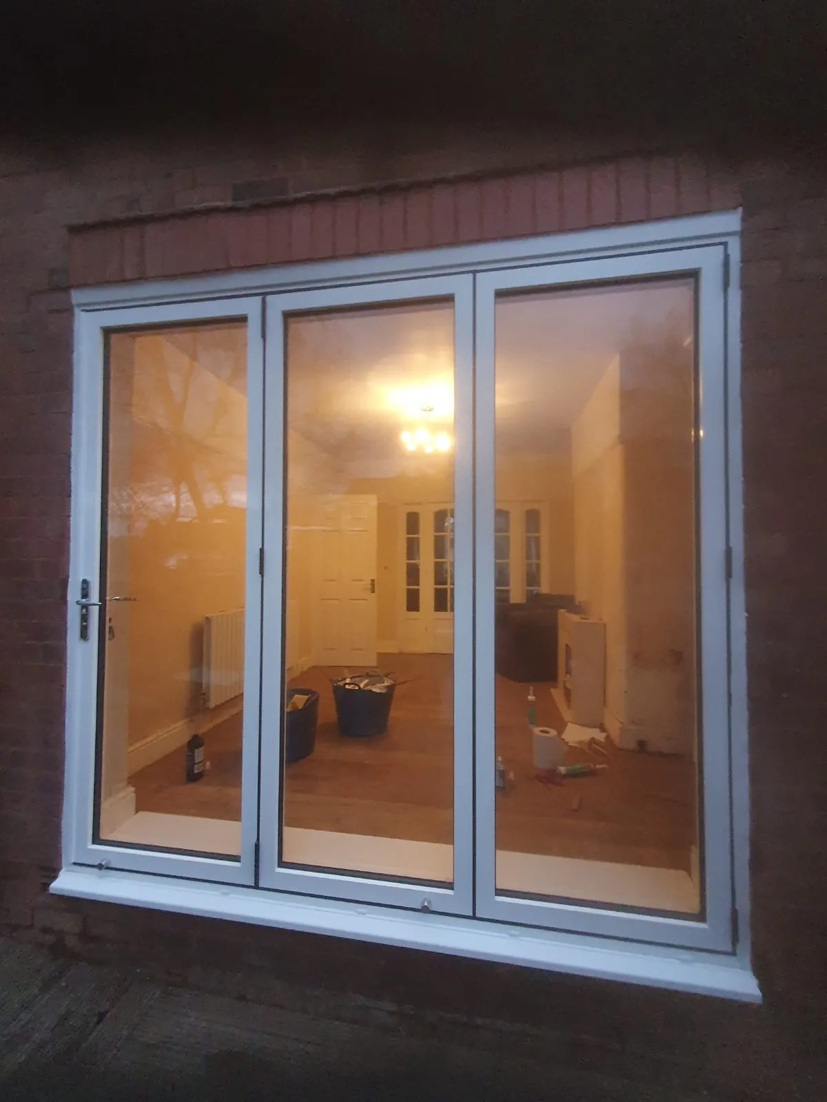 White three-panel aluminium patio doors illuminated at night on a brick property